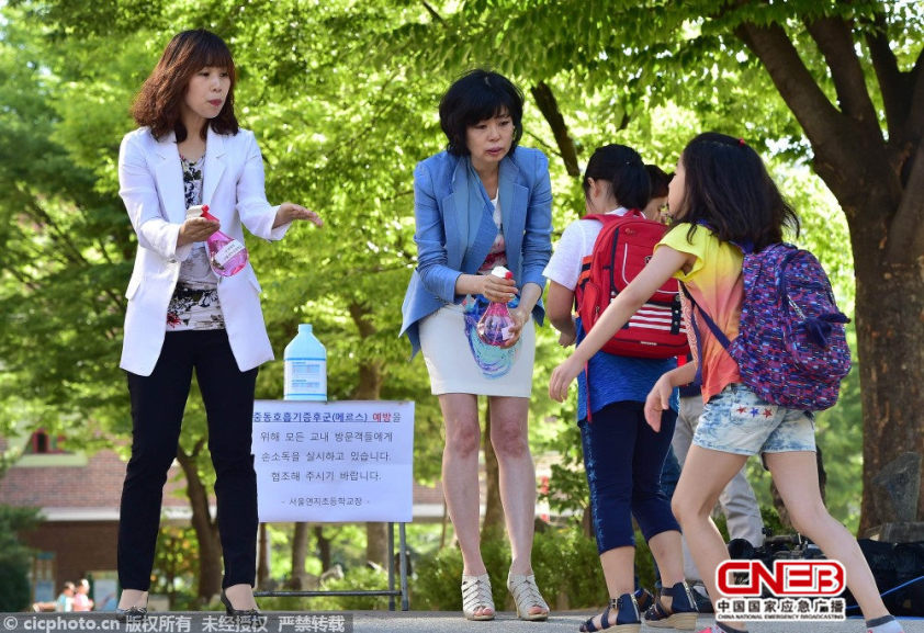 韩国学校工作人员为小学生喷洒消毒剂。