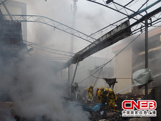爆炸现场弥漫着大量浓烟，部分厂房坍塌，消防官兵正在扑救。
